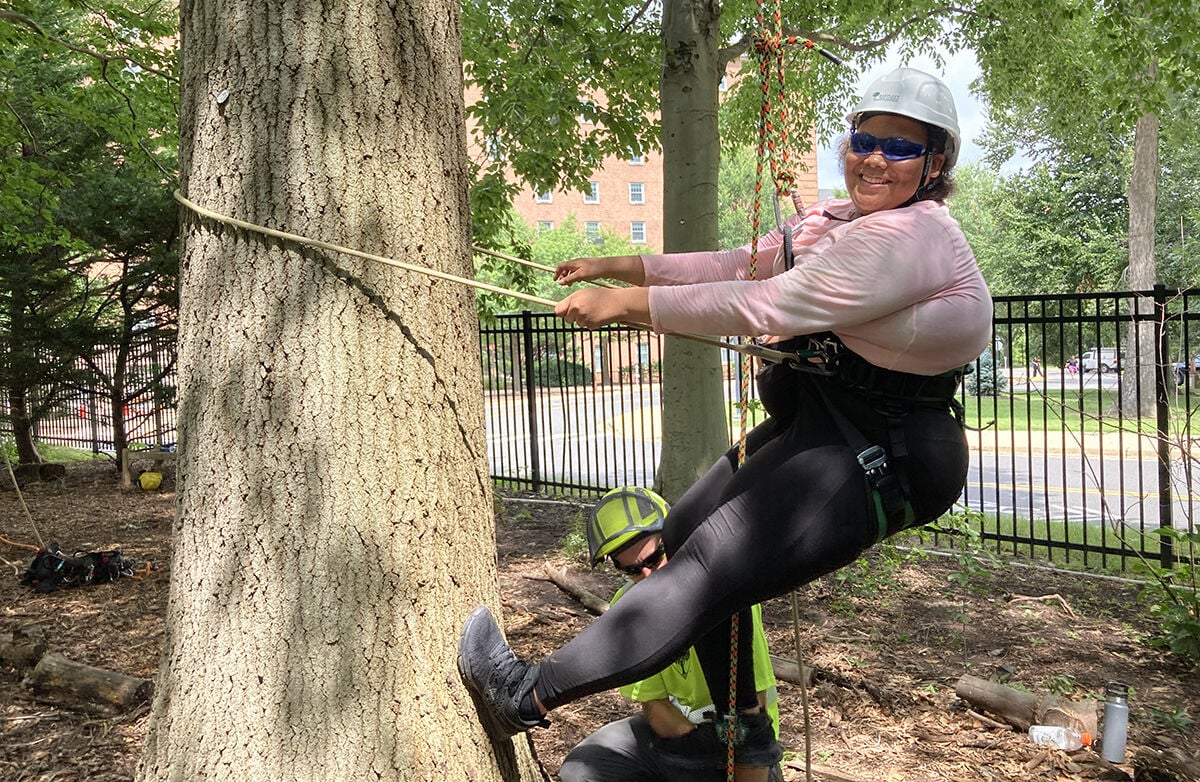 Nevaeh Murphy of Bladensburg flashes a smile after getting off the ground on her second try scaling an oak tree during an Urban Forestry Careers Camp this summer. (Photo by Timothy B. Wheeler/Chesapeake Bay Journal)